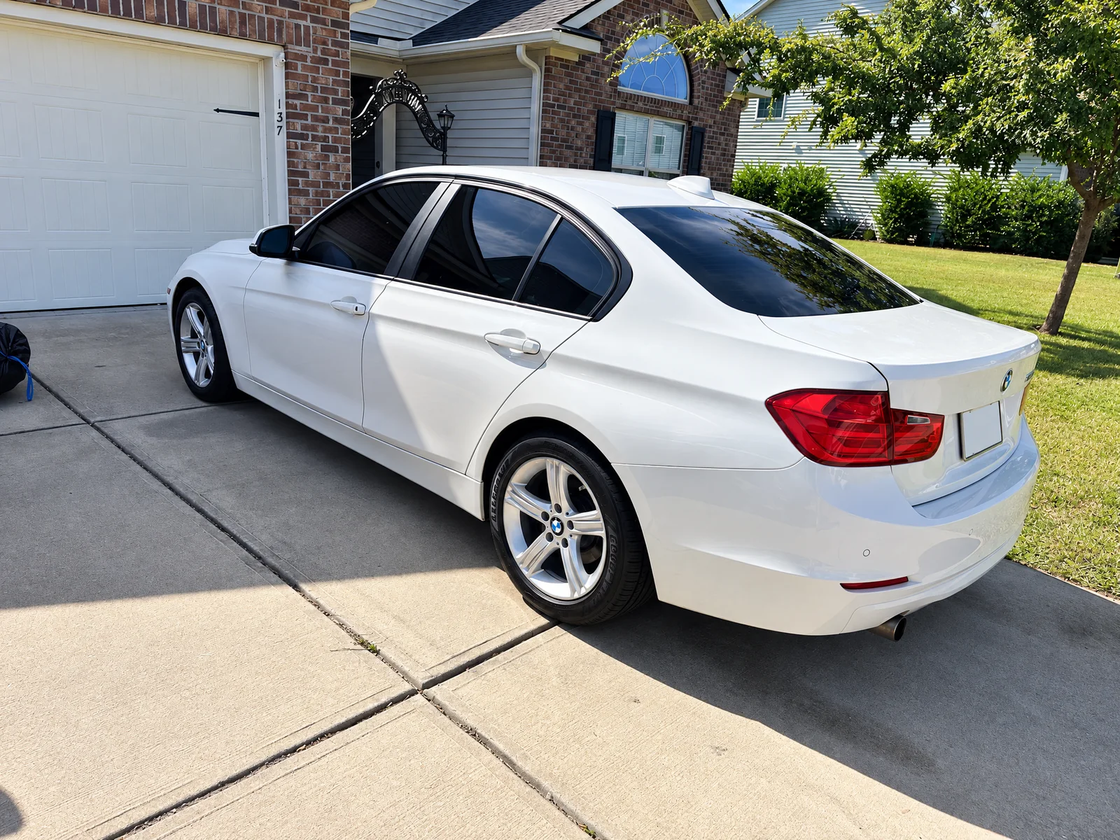 A white BMW 3 Series with dark tinted side and rear windows on a driveway