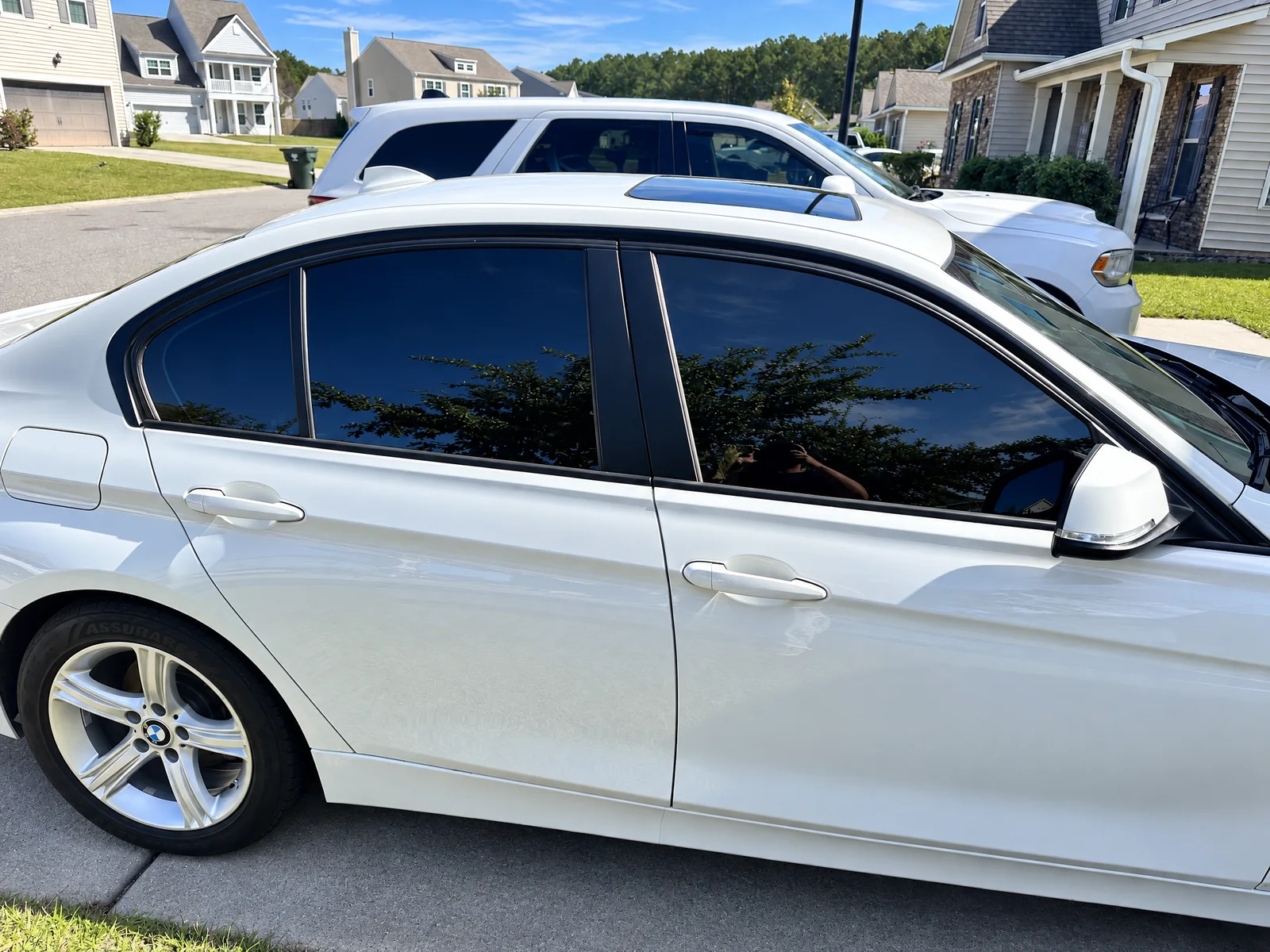 A white BMW 3 Series side windows, tinted dark with tree reflections
