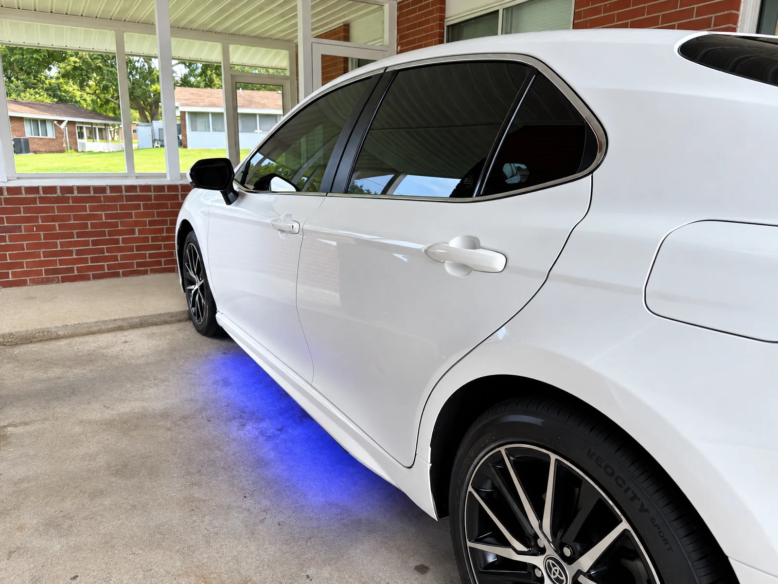 A white Toyota Camry with tinted rear windows under a carport